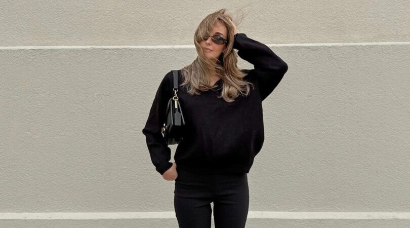 Een vrouw die poseert voor een witte muur in een compleet zwarte outfit.