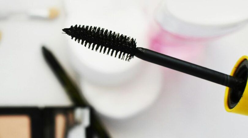 Mascaraborsteltje boven een witte tafel met andere beautyproducten.