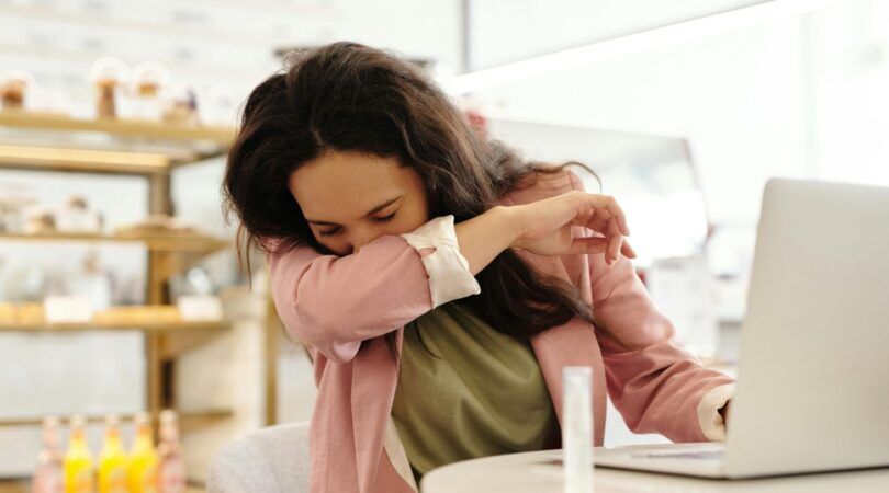 Vrouw niest in ellenboog achter laptop