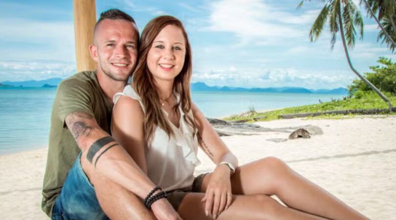 Jongen en meisje zitten tegen elkaar aan op een strand.