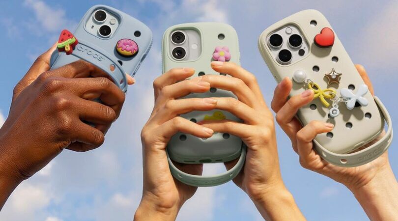 Drie verschillende telefoonhoesjes worden vastgehouden door drie verschillende armen. De telefoonhoesjes zijn van het merk: Crocs in samenwerking met SLBS.