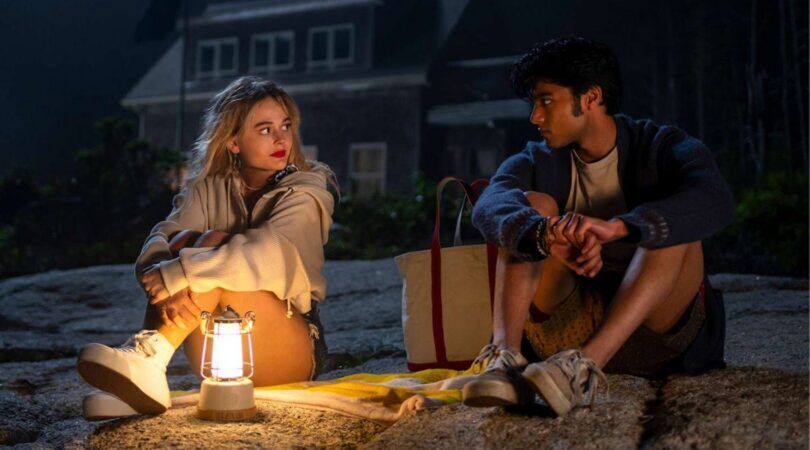 Een man en vrouw zitten op het strand in het donker. Er brandt een lantaarn. Afbeelding uit: We Were Liars.