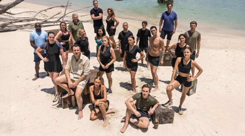 Expeditie Robinson deelnemers staan op een tropisch eiland. Ze kijken stoer omhoog.
