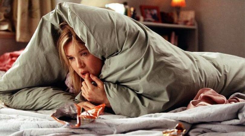Bridget Jones ligt onder de dekens iets te eten.