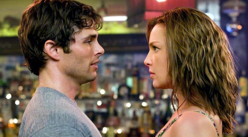 De twee hoofdkarakters van 27 Dresses kijken elkaar intens aan.