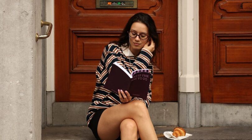 Meisje zit op een trap voor een voordeur. Ze leest Het Solo Date Journal- Solo is the way to go.