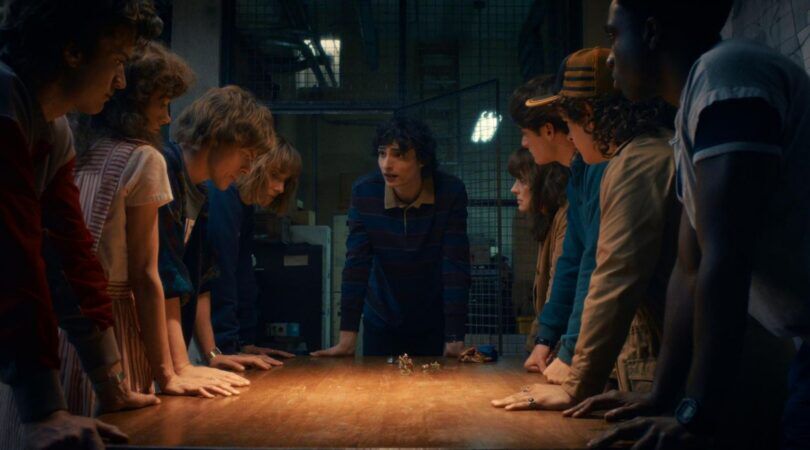 De personages uit Stranger Things staan aan een tafel.