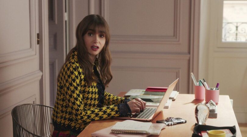 Emily uit Emily in Paris zit achter haar bureau.