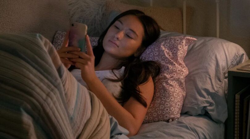 Een jonge vrouw ligt in bed naar haar telefoon te staren.