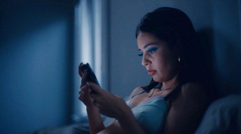 Een vrouw zit in bed in het donker. Ze kijkt naar haar telefoon. Foto uit de HBO-serie: Euphoria.