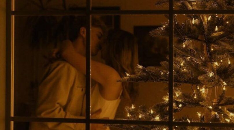 Foto van stelletje dat zoent bij een kerstboom. Ze staan achter een raam.