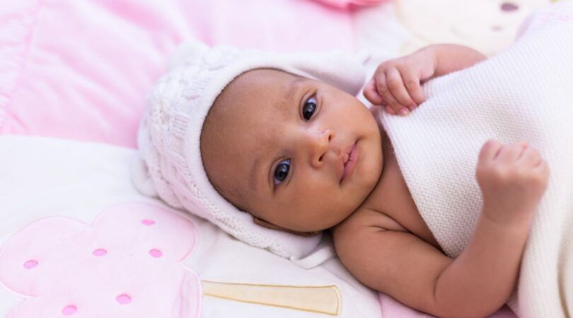 Foto van babymeisje. Ze ligt in een roze bedje.