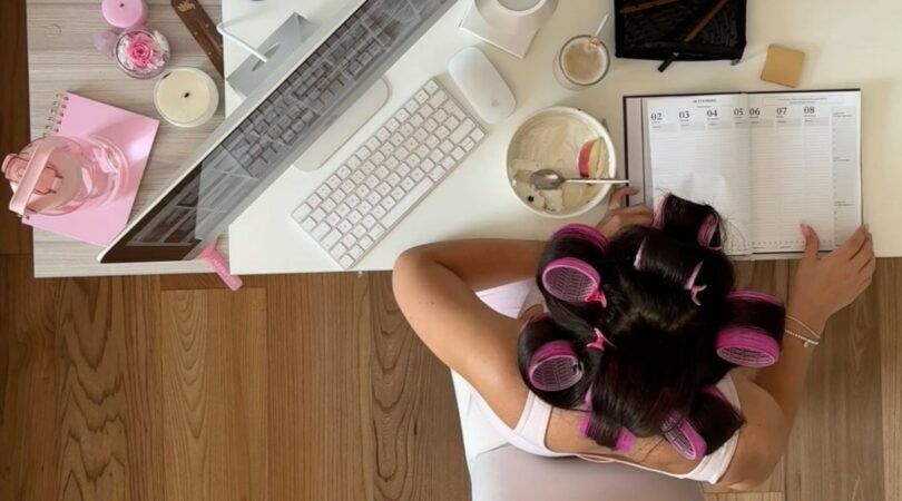 Foto van studente achter haar bureau. Ze schrijft iets in haar notititeblok. Ze heeft krulspelden in haar haren.