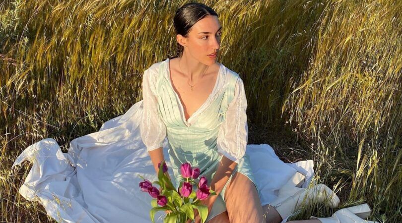 Meisje zit op een kleedje in het gras.