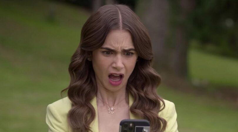 Emily, uit Emily in Paris, kijkt verbaasd naar haar telefoon.