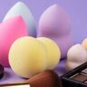 Beautyblenders en andere make-up producten op een paarse achtergrond.