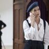 Een vrouw in een wit overhemd met een baret op, belt aan de telefoon.