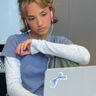 Meisje zit achter een laptop. Ze kijkt verdrietig voor zich uit.