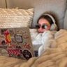 Vrouw in bed met haar laptop, bril en koptelefoon.